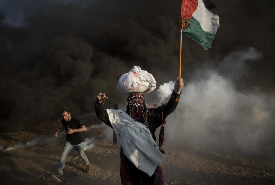 Palestinian protesters run for cover from teargas fired by Israeli troops during a protest at the Gaza Strip's border with Israel, Friday, Oct. 12, 2018. (AP Photo/Khalil Hamra)