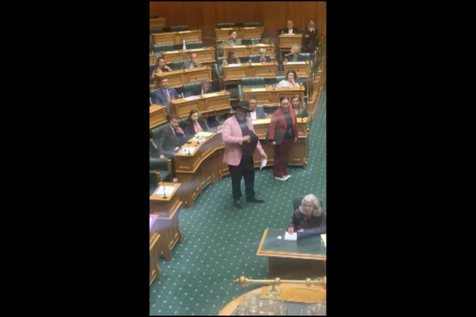 In this image from video, Indigenous New Zealand lawmaker Rawiri Waititi, center, performs a Maori haka in Parliament in Wellington, New Zealand, Wednesday, May 12, 2021. Waititi was thrown out of Parliament's debating chamber for performing a Maori haka in protest at what he said were racist arguments. Waititi's stance came after ongoing debate among lawmakers about the government's plans to set up a new Maori Health Authority as part of sweeping changes to the health care system. His party's other co-leader, Debbie Ngarewa-Packer is seen at right. (Thomas Coughlan via AP)