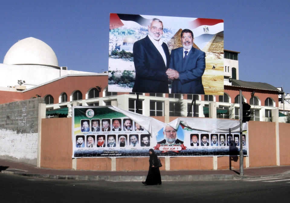 FILE - In this Saturday, Aug. 25, 2012 file photo, a Palestinian woman walks past a poster of Gaza's Hamas Prime Minister Ismail Haniyeh, left, and Egyptian President Mohammed Morsi in Gaza City. An Egyptian court ruled on Tuesday, March 4, 2014 to ban activities of the Palestinian militant group Hamas in Egypt in a move likely to fuel tension between Cairo's military-backed government and the Islamic group that rules the neighboring Gaza Strip. Egypt's interim leaders maintain that Hamas is playing a key role in the insurgency by militants in the northern region of the Sinai Peninsula, which borders Hamas-ruled Gaza and Israel. (AP Photo/Hatem Moussa, File)