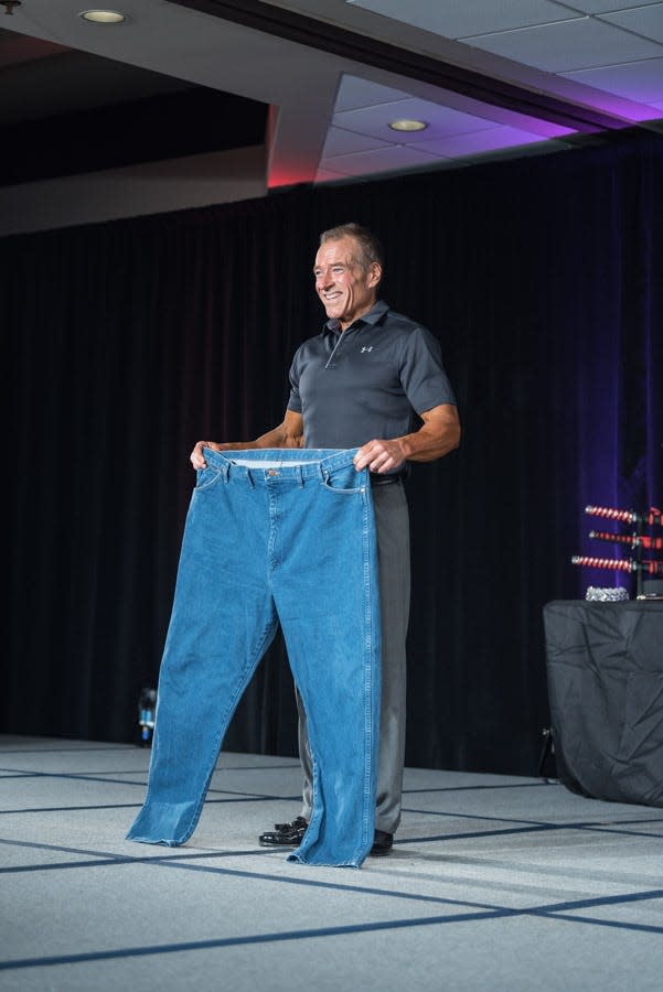 Athlete Ken Jones smiling onstage as he holds a pair of pants that used to fit him before he lost more than 100 pounds.