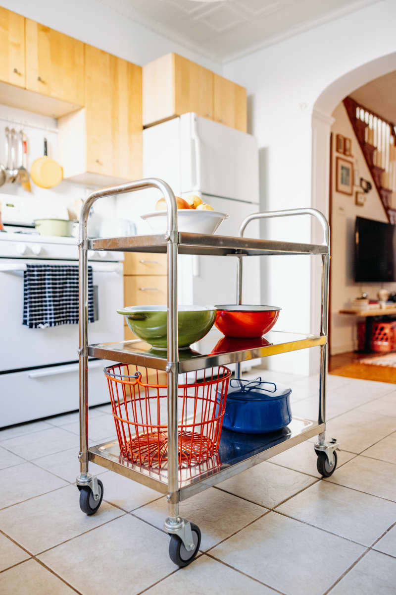 Storage cart holds colorful cookware in white kitchen.