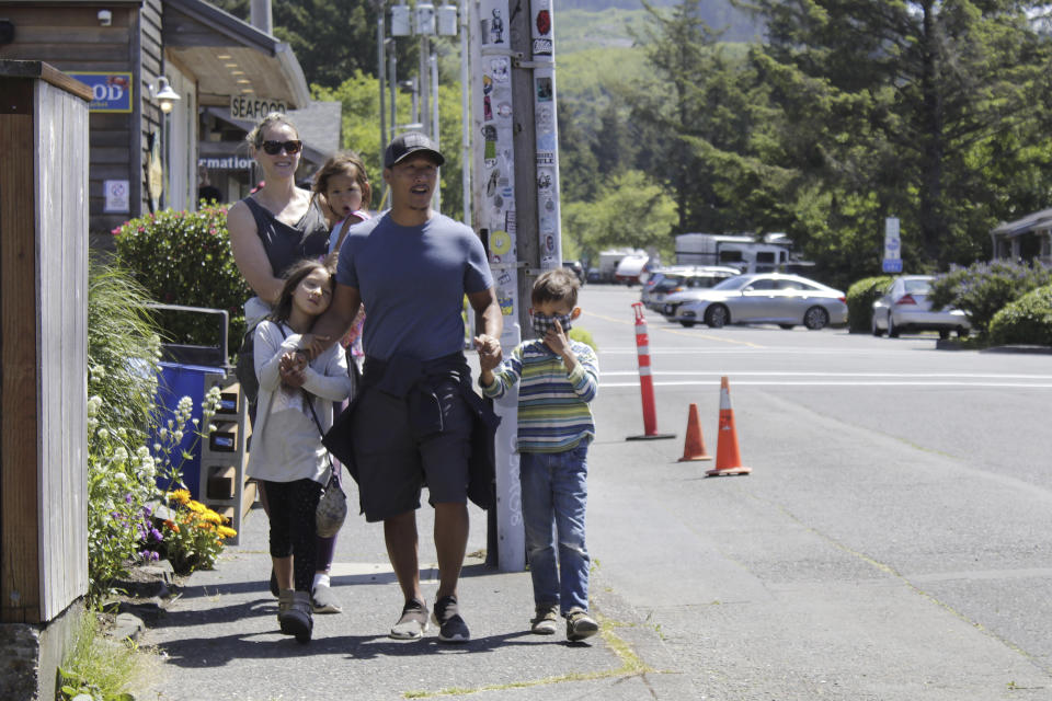 In this Thursday, May 28, 2020, photo, tourists Tuan Nguyen and his wife, Sarah Nguyen, walk with their children, twins Lukas and Lauren, 7, and Alyssa, 4, as they walk through downtown in Cannon Beach, Ore. The Nguyens were visiting from the Portland, Ore., suburbs but elected to stay in their RV instead of a hotel to feel safer from the coronavirus. (AP Photo/Gillian Flaccus)