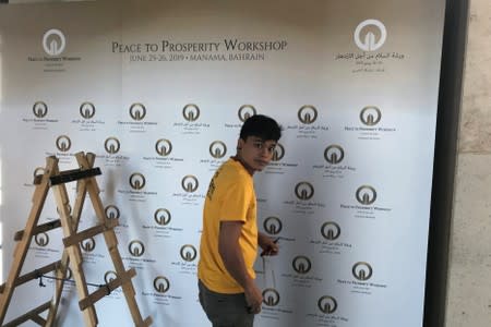 A worker places a banner at the pavilion where the U.S. hosted event "Peace to Prosperity" takes place outside Four Seasons Hotel in Manama