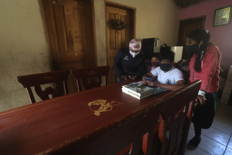 Con mascarilla para frenar la propagación del nuevo coronavirus, Perla Iguamba, directora de la escuela municipal de Cayambe, utiliza su celular para ayudar a dos de sus estudiantes a conectarse, con su celular, a las clases virtuales desde su casa, en La Josefina, Ecuador, el 3 de septiembre de 2020. Los alumnos habían intentado conectarse con el servicio de internet de su casa, pero un apagón en el pueblo obligó a Iguamba a echarles una mano con su propio celular. (AP Foto/Dolores Ochoa)