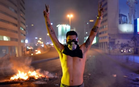 A protester flashes victory signs in front a fire set by protesters to block a road during a protest in Beirut,  - Credit: EPA