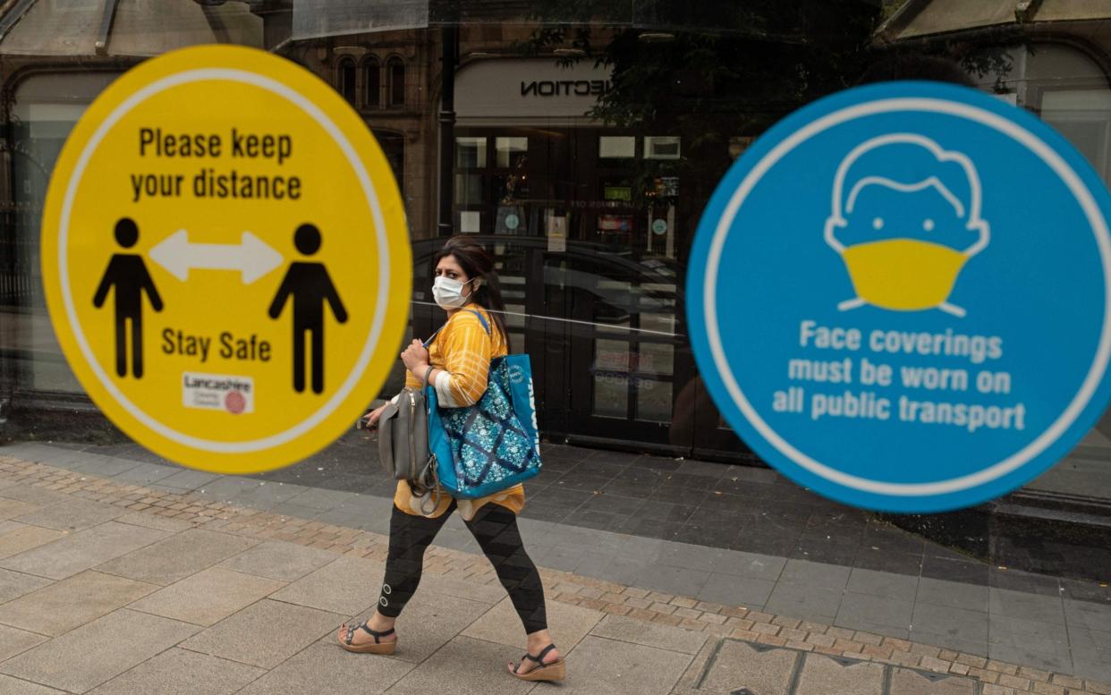 A woman walks past health advisory signs in Preston, Lancashire, where local restrictions have been imposed - Oli Scarff/AFP