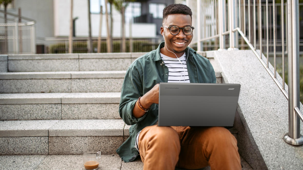  A man sitting on outside steps using an Acer Chromebook Plus 514 . 