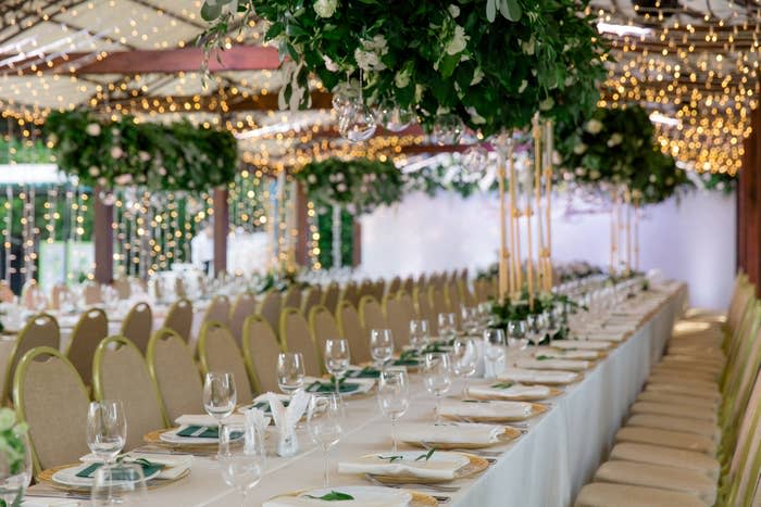 Elegant wedding reception setup with long tables, plush chairs, hanging greenery, and string lights, creating a romantic and festive atmosphere