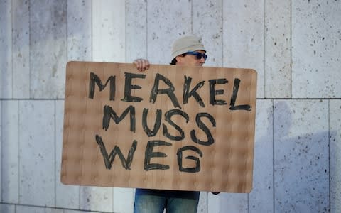 A protestor holds a placard reading "Merkel must go" outside the CDU headquarters  - Credit: REUTERS/Axel Schmidt