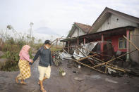 Villagers walk near their damaged home in an area affected by the eruption of Mount Semeru in Lumajang, East Java, Indonesia, Sunday, Dec. 5, 2021. The highest volcano on Indonesia’s most densely populated island of Java spewed thick columns of ash, searing gas and lava down its slopes in a sudden eruption triggered by heavy rains on Saturday. (AP Photo/Trisnadi)