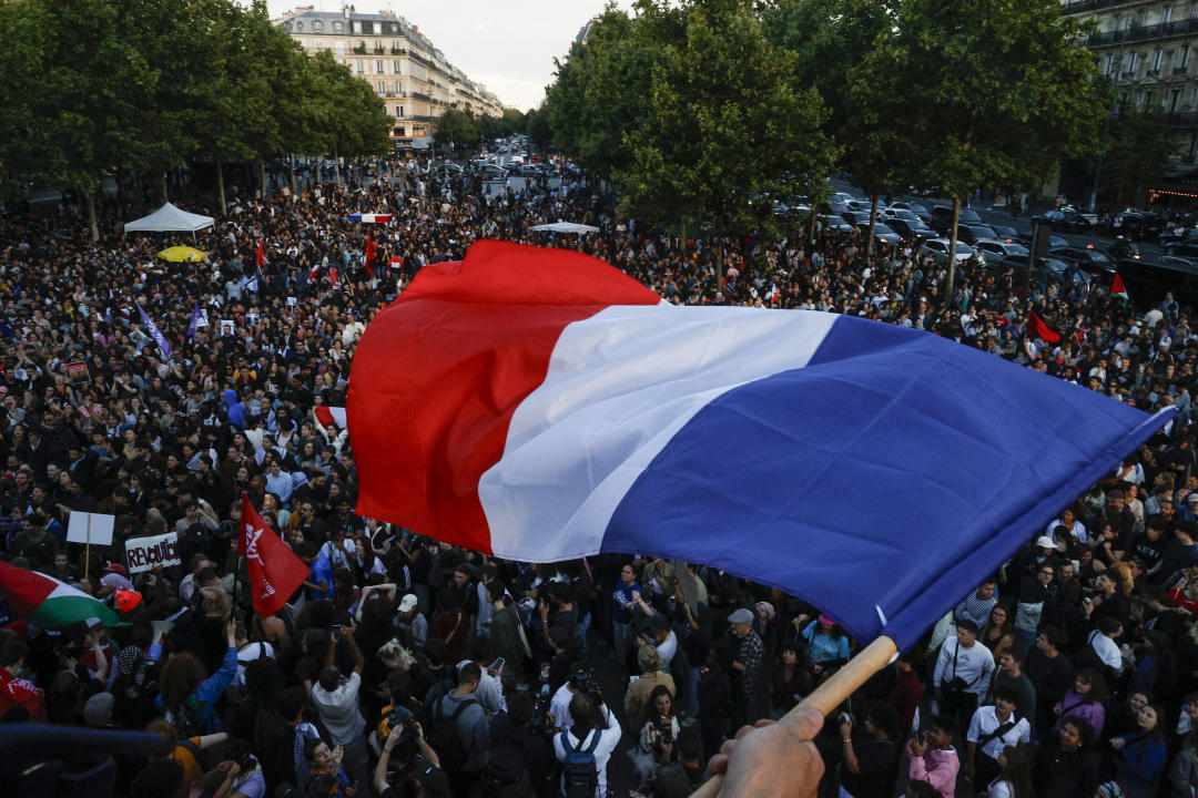 A protester hold a French flag as people gather at the Place de la Republique after partial results in the second round of the early French parliamentary elections, in Paris, France, July 7, 2024. REUTERS/Abdul Saboor