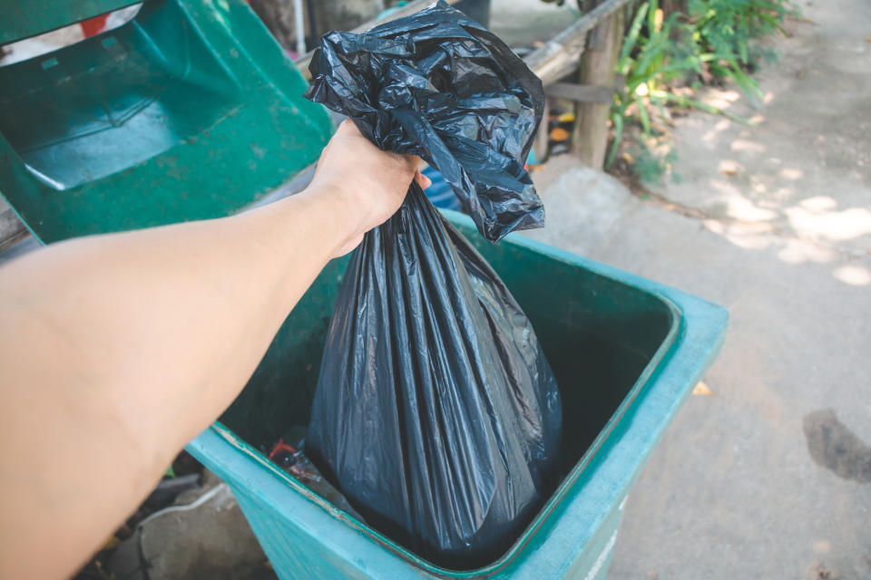 A person places a black garbage bag in a bin. A woman in England was arrested for using the wrong bin bags. She used black ones instead of clear and orange ones to separate her waste.