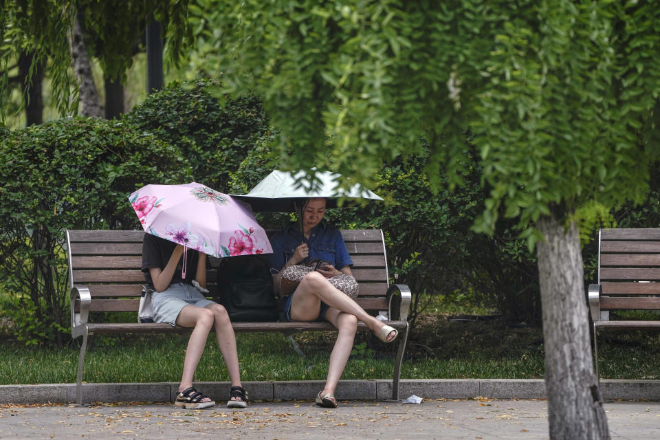 Dos mujeres se cubren del sol durante un día caluroso en Beijing, el lunes 3 de julio de 2023. (AP Foto/Andy Wong)