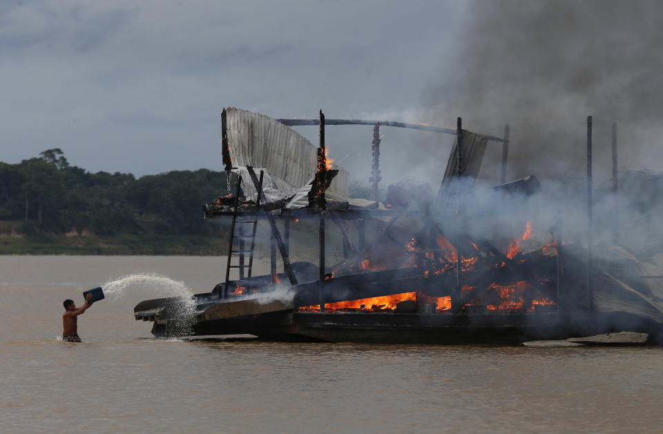 ARCHIVO - Un minero ilegal lanza agua sobre una pila de barcazar en llamas en un afluente del río Amazonas, en el estado de Amazonas, Brasil, el 28 de noviembre de 2021. (AP Foto/Edmar Barros, Archivo)