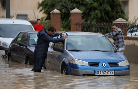 People are seen next to a partially submerged car as torrential rains hit Orihuela