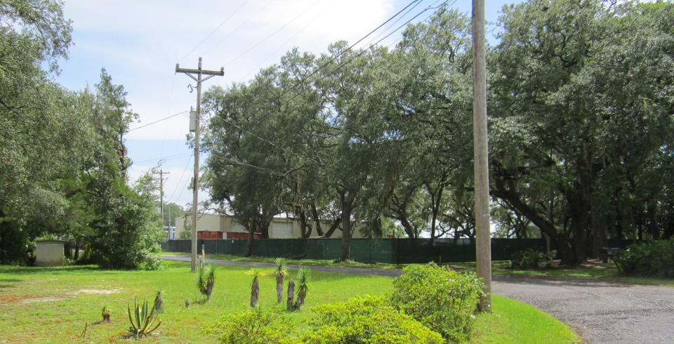 Picture from the road, through telephone poles, trees and fencing, of the maritime company that officially employed Stanek and the other crew members.