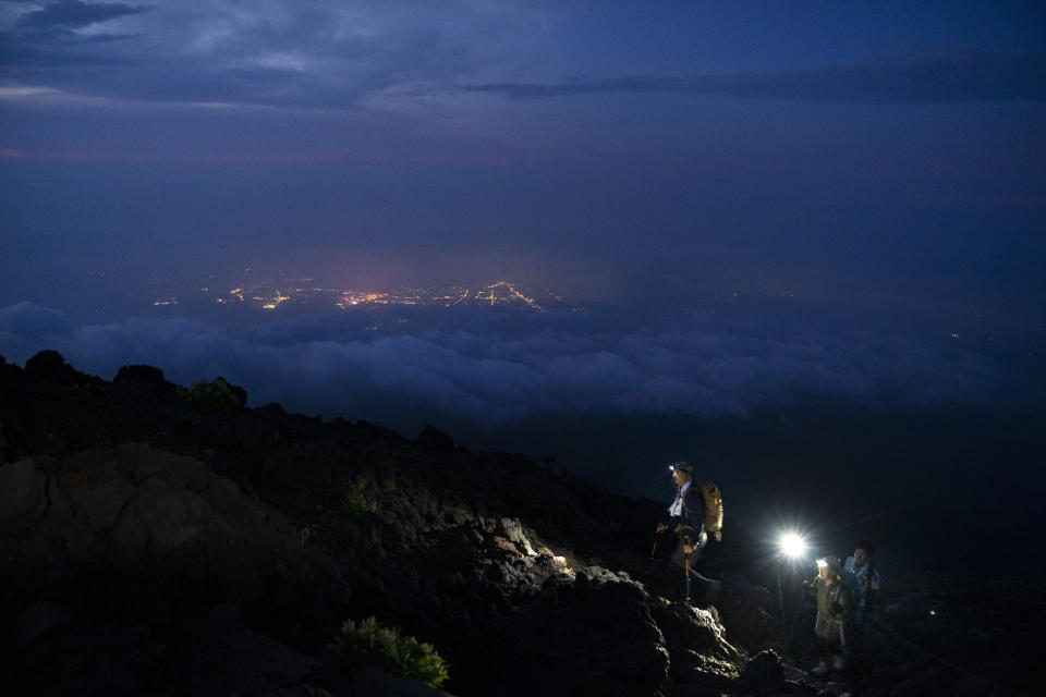 Climbers make their way along the Yoshida trail toward the summit of Mount Fuji as the glow from the town's lights are visible through clouds Friday, Aug. 2, 2019, in Japan. (AP Photo/Jae C. Hong)