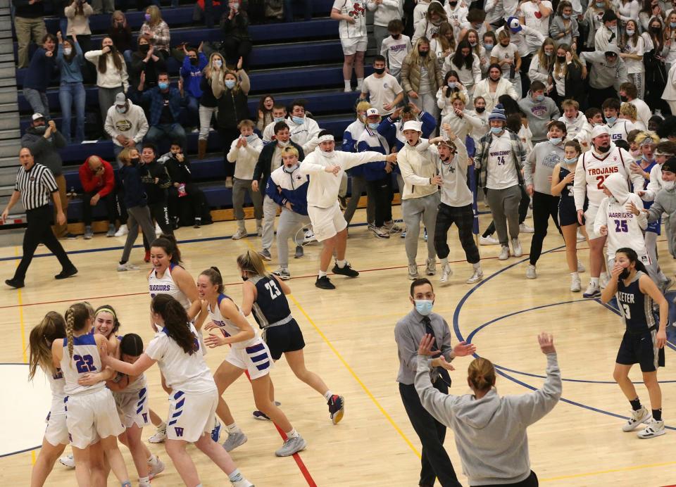 Winnacunnet's Abby Wilber is hugged by teammates as the Warrior student section storms the court after Wilber's half-court buzzer-beating shot beat Exeter, 42-40.