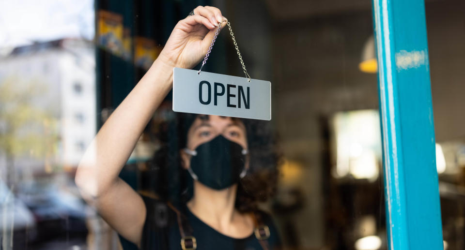 Young non-binary person hanging an open sign from the door of a small bakery. Source: Getty Images