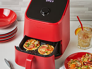 The Instant Vortex mini having just cooked two small pizzas, more pizzas, plates and a beverage on side