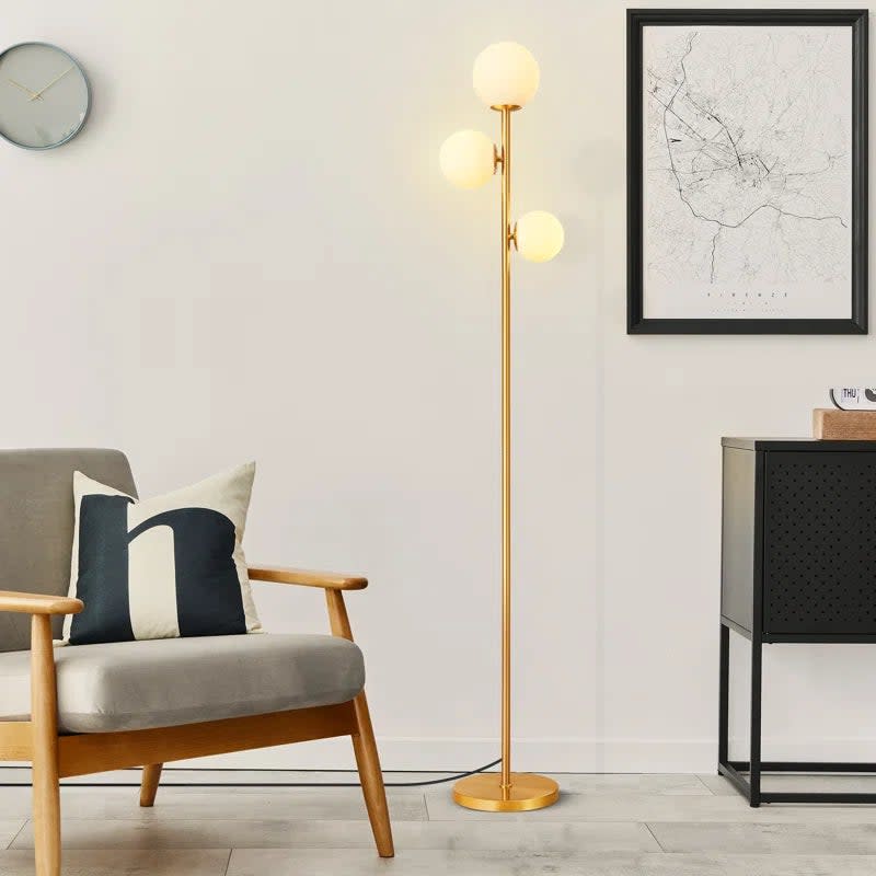 The floor lamp with three globes beside a chair and a sideboard in a living room setting
