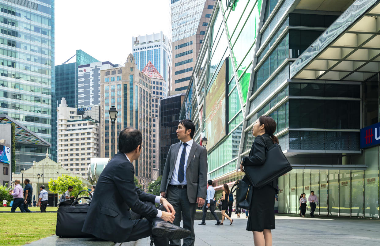 Image shows two men and women in suits looking up at the buildings in Raffles Place. (PHOTO: Getty)