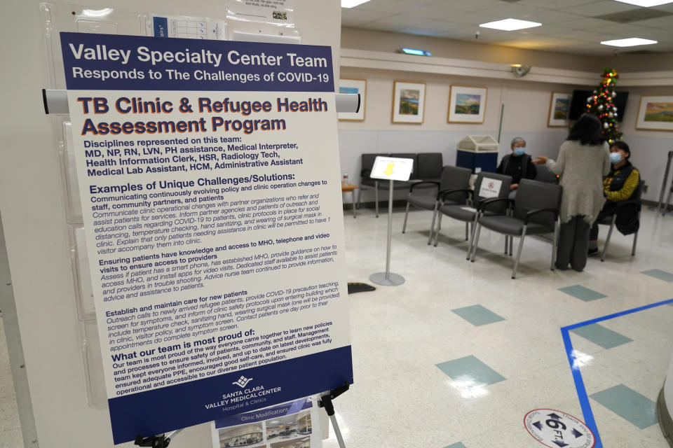 A sign about COVID-19 is displayed in a waiting room at the Valley Health Center TB/Refugee Program in San Jose, Calif., Thursday, Dec. 9, 2021. The staff of Silicon Valley's decades-old refugee health clinic may not all speak the language of the Afghan refugees starting new lives in the San Francisco Bay Area. But they know the anxiety and stress of newcomers who fled war and chaos to end up in a country where they don't speak the language and everything is different. (AP Photo/Eric Risberg)