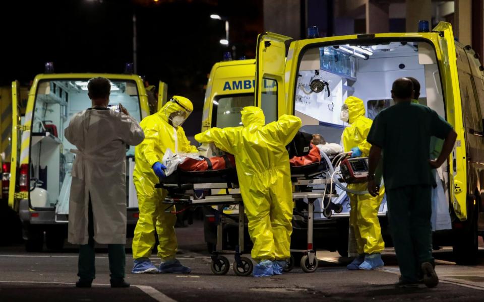 A patient being tranfered from an ambulance by staff in bright yellow PPE - Duarte Sa/Reuters