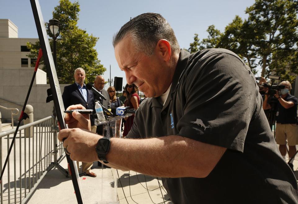 Sheriff Alex Villanueva, wearing a Dodgers polo, signing a whiteboard with a marker