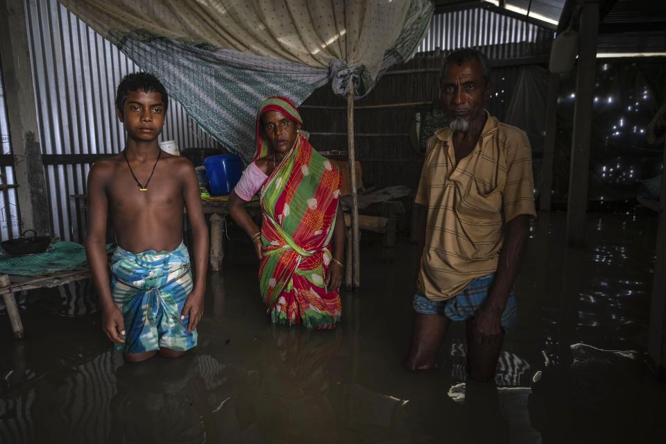 Yaad Ali, 55, right, and his wife Monuwara Begum, 45, center, and Musikur Alam, 14, stand in their submerged house in Sandahkhaiti, a floating island village in the Brahmaputra River in Morigaon district, Assam, India, Wednesday, Aug. 30, 2023. (AP Photo/Anupam Nath)