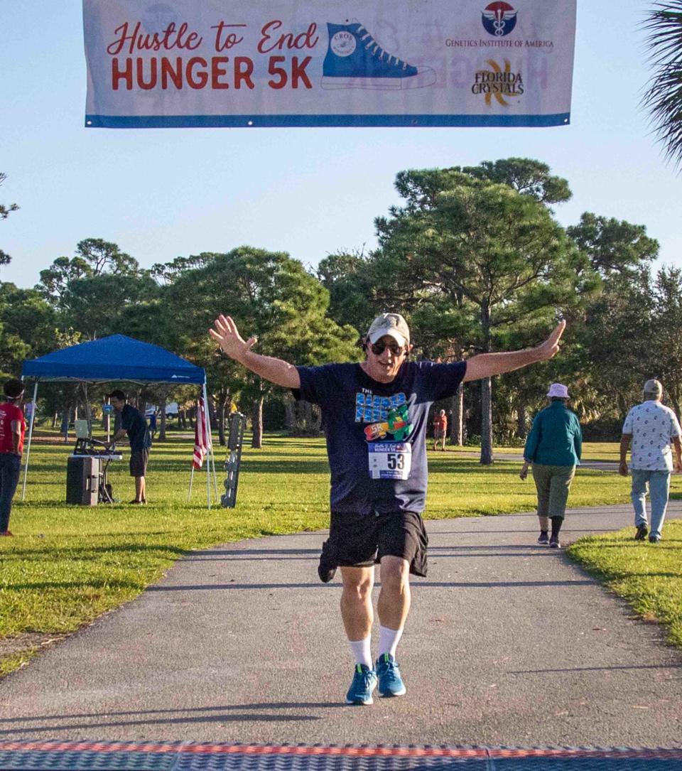 Rich Pollack raises his hands just before crossing the finish line of the Hustle to End Hunger 5K race at John Prince Park on Oct. 7.