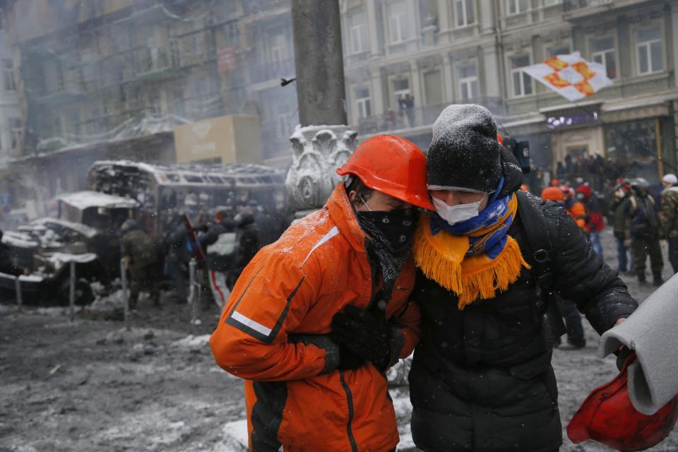 A wounded protester, left, is assisted by a fellow protester during clashes with police in central Kiev, Ukraine, early Wednesday, Jan. 22, 2014. At least two people have died in clashes between protesters and police in the Ukrainian capital Wednesday, according to medics on the site, in a development that will likely escalate Ukraine's two month-long political crisis. (AP Photo/Sergei Grits)