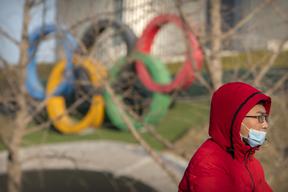 A man wearing a face mask to protect against the spread of the coronavirus rides a bicycle pas the Olympic rings at the base of the Olympic Tower in Beijing, Tuesday, Feb. 2, 2021. A small core of international lawyers and activists are prodding leading Olympic sponsors to acknowledge China's widely reported human-rights abuses against Muslim Uyghurs, Tibetans and other minorities. (AP Photo/Mark Schiefelbein)