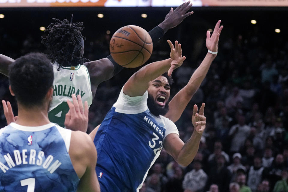 Minnesota Timberwolves forward Karl-Anthony Towns, right, passes the ball while pressured by Boston Celtics guard Jrue Holiday (4) during the second half of an NBA basketball game Wednesday, Jan. 10, 2024, in Boston. (AP Photo/Charles Krupa)