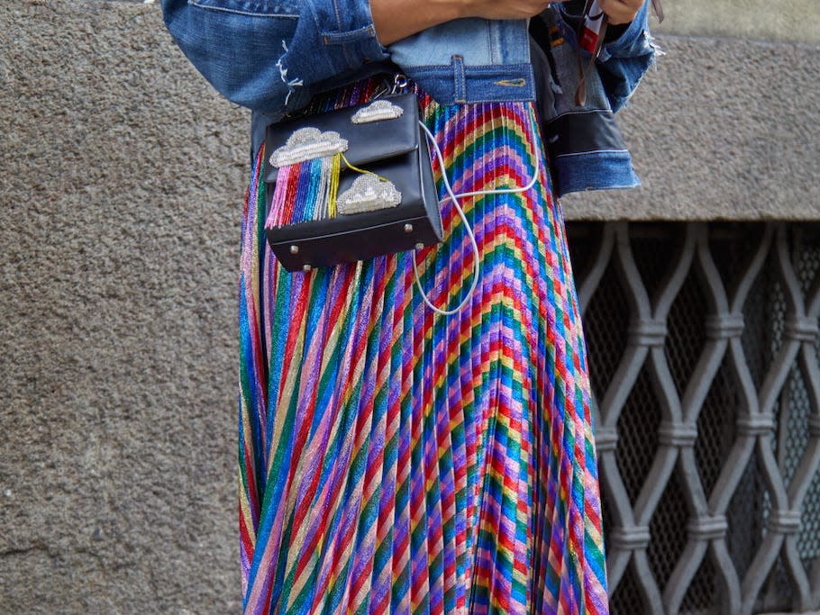 person looking at their phone on a sidewalk wearing a jean jacket and a rainbow, metallic pleated skirt
