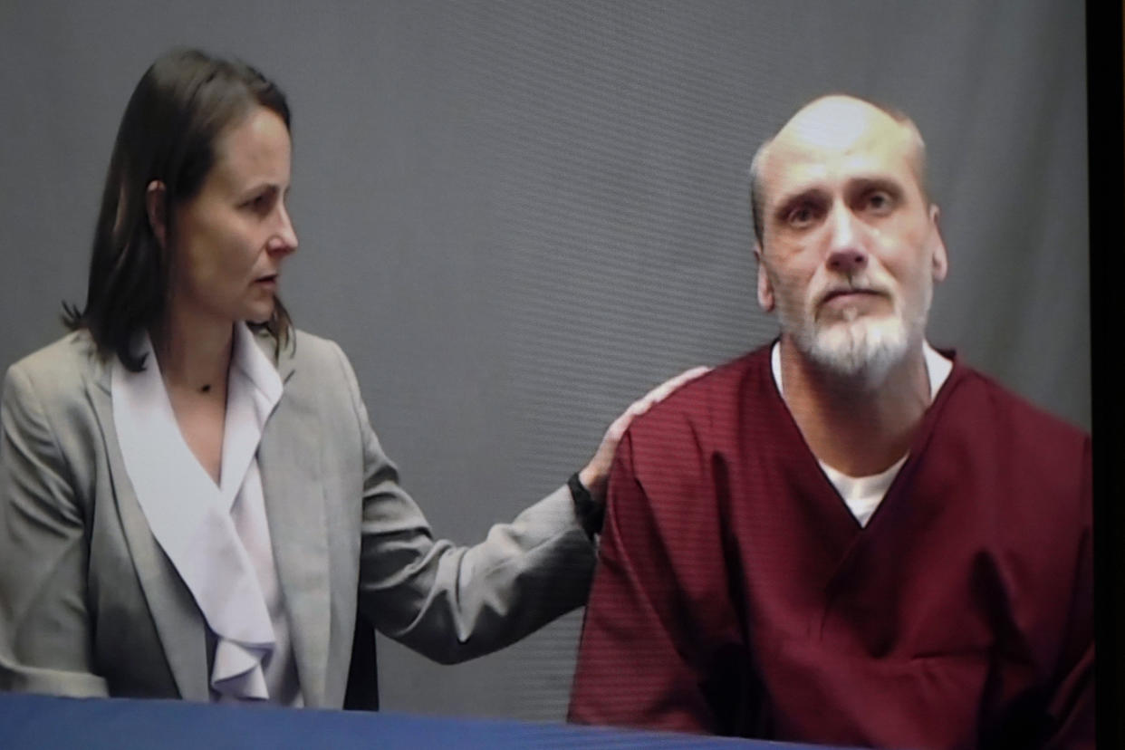 Julie Gardner, in profile, sits facing James Coddington with her hand on his shoulder as he faces the camera.