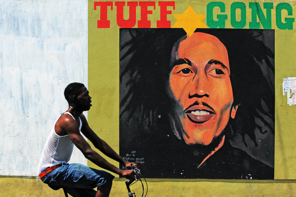 A man pedals past a mural of late musician Bob Marley in Kingston on February 8, 2009. Marley, who was born in 1945 and died in 1981, remains the most widely known and revered performer of reggae music and is also credited for helping spread Jamaican music to a worldwide audience. Marley's best known hits include "I Shot the Sheriff", "No Woman, No Cry", "Exodus", "Could You Be Loved", "Stir It Up", "Jamming", "Redemption Song", "One Love" and together with The Wailers "Three Little Birds", as well as the posthumous releases "Buffalo Soldier" and "Iron Lion Zion." The compilation album, Legend, released in 1984, three years after his death, is the best-selling reggae album ever with sales of more than 20 million copies.       AFP PHOTO/Jewel SAMAD (Photo credit should read JEWEL SAMAD/AFP via Getty Images)