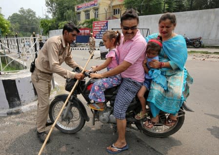 An Indian policeman stops a motorbike at a check point along a road during restrictions in Jammu