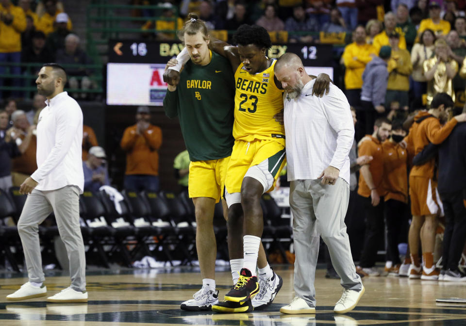 FILE - Baylor forward Jonathan Tchamwa Tchatchoua (23) is helped from the court as he leaves the game with an apparent leg injury during the first half of an NCAA college basketball game against Texas on Saturday, Feb. 12, 2022, in Waco, Texas. Tchamwa Tchatchoua sees himself as a “walking miracle” after getting back on the court for 14th-ranked Baylor nearly a full year after a gruesome knee injury that many people thought would end his career. (AP Photo/Ray Carlin, File)