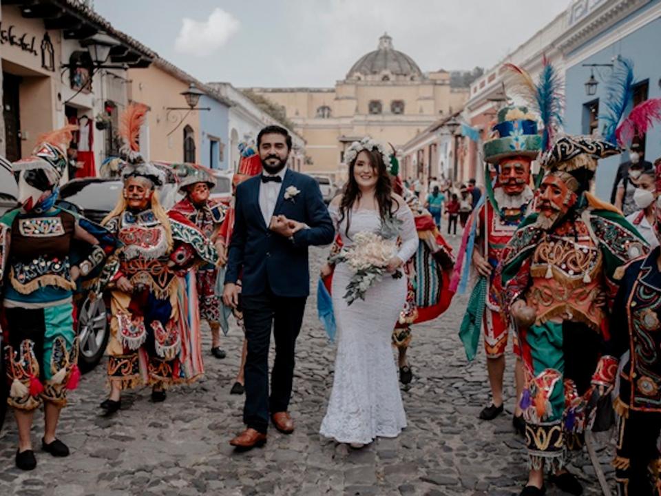 A bride and groom walk between a group of men dressed in traditional Guatemalan garb.