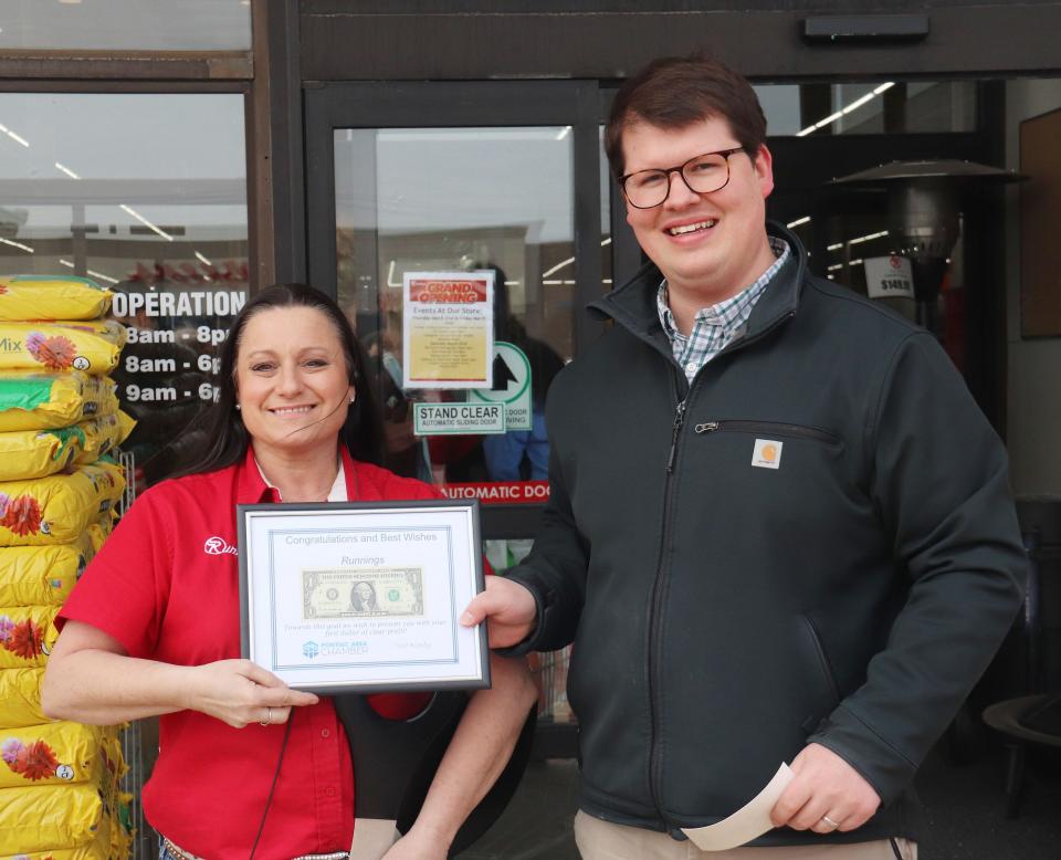 Pontiac Area Chamber of Commerce President Drew Keller of the State Bank of Graymont gives Runnings store manager Bridget Reaves a framed dollar bill recognizing the first dollar the store took in after opening.