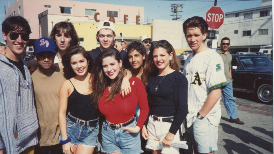 A still from the documentary Kid 90 in which nine teens are stood smiling at the camera.