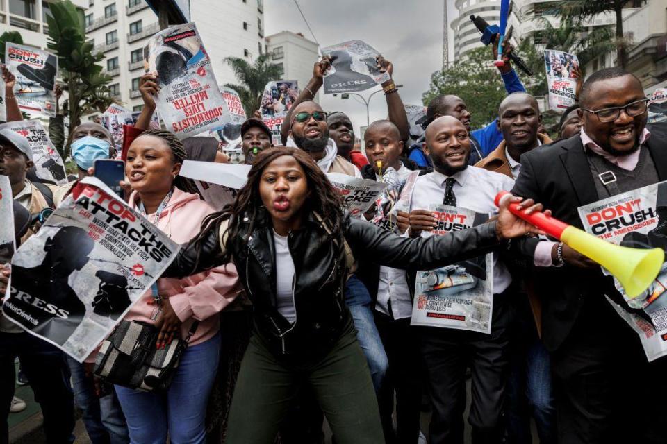 People sing and hold signs.  A woman at the front of the group does a vuvuzela in Nairobi, Kenya - Wednesday, July 24, 2024