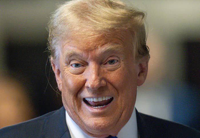 Donald Trump smiling, showing his teeth, wearing a dark suit and white shirt