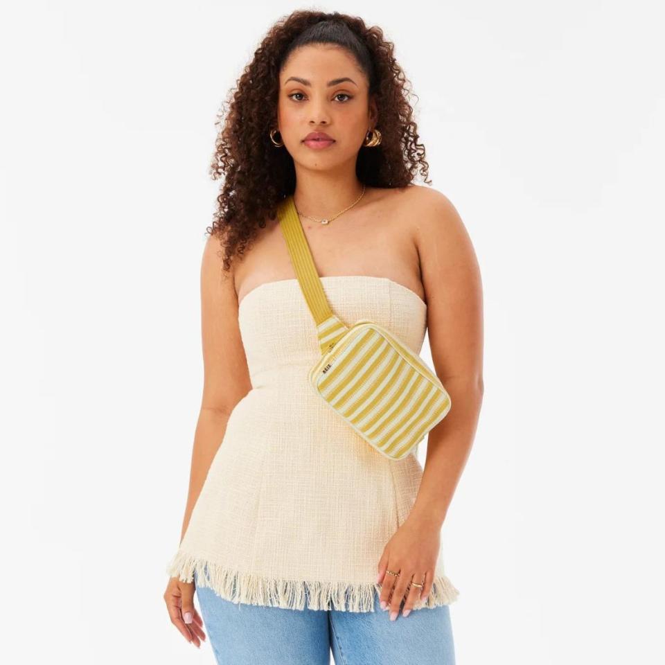 model wearing yellow and white striped beis belt bag with fringe white top