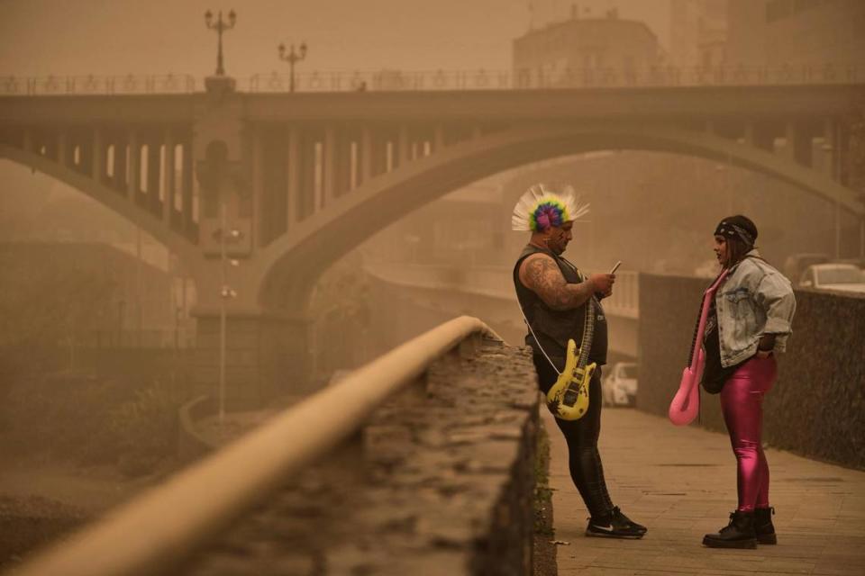 Dos personas vestidas de carnaval permanecen bajo una nube de polvo rojo en Santa Cruz de Tenerife, España, el domingo 23 de febrero de 2020.