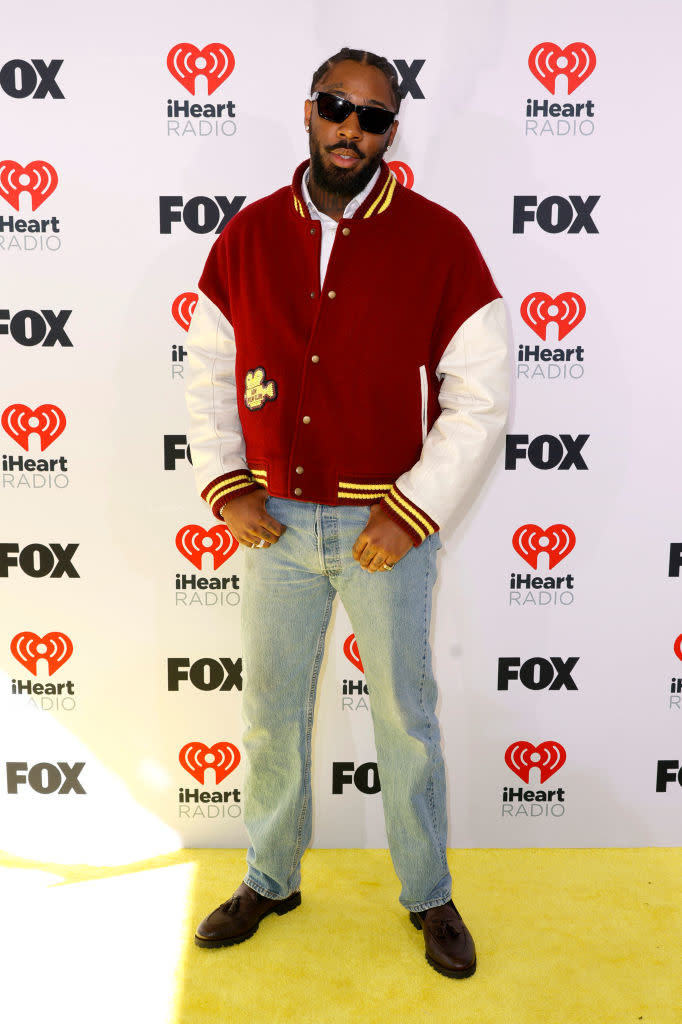 Person in a varsity jacket and jeans poses on a yellow event carpet