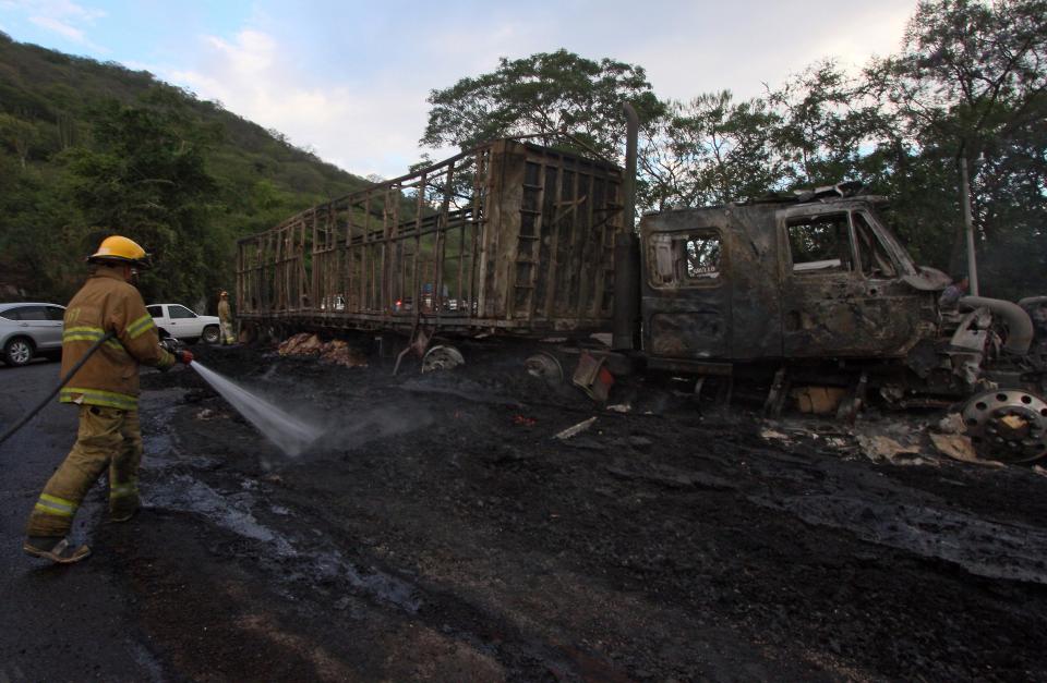 Firefighters work on a burned truck in the Guadalajara - Autlan highway, Jalisco state, Mexico, on May 1, 2015. More than a dozen vehicles were set on fire on Friday across Guadalajara, Mexico's second biggest city, while a drug gang and authorities clashed in another part of Jalisco state. Authorities have not said who was responsible for the violence, but it came amid an escalation of violence by the Jalisco New Generation Drug Cartel, which killed 20 police officers in two ambushes in March and April.    AFP PHOTO/Hector Guerrero        (Photo credit should read HECTOR GUERRERO/AFP via Getty Images)