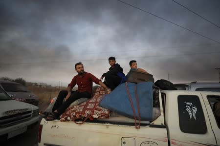 People sit on belongings at a back of a truck as they flee Ras al Ain town