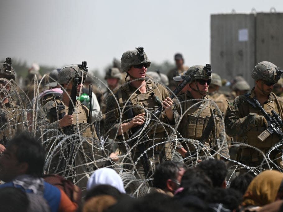 US soldiers stand guard behind barbed wire as Afghans sit on a roadside near the military part of the airport in Kabul on August 20, 2021, hoping to flee from the country after the Taliban's military takeover of Afghanistan